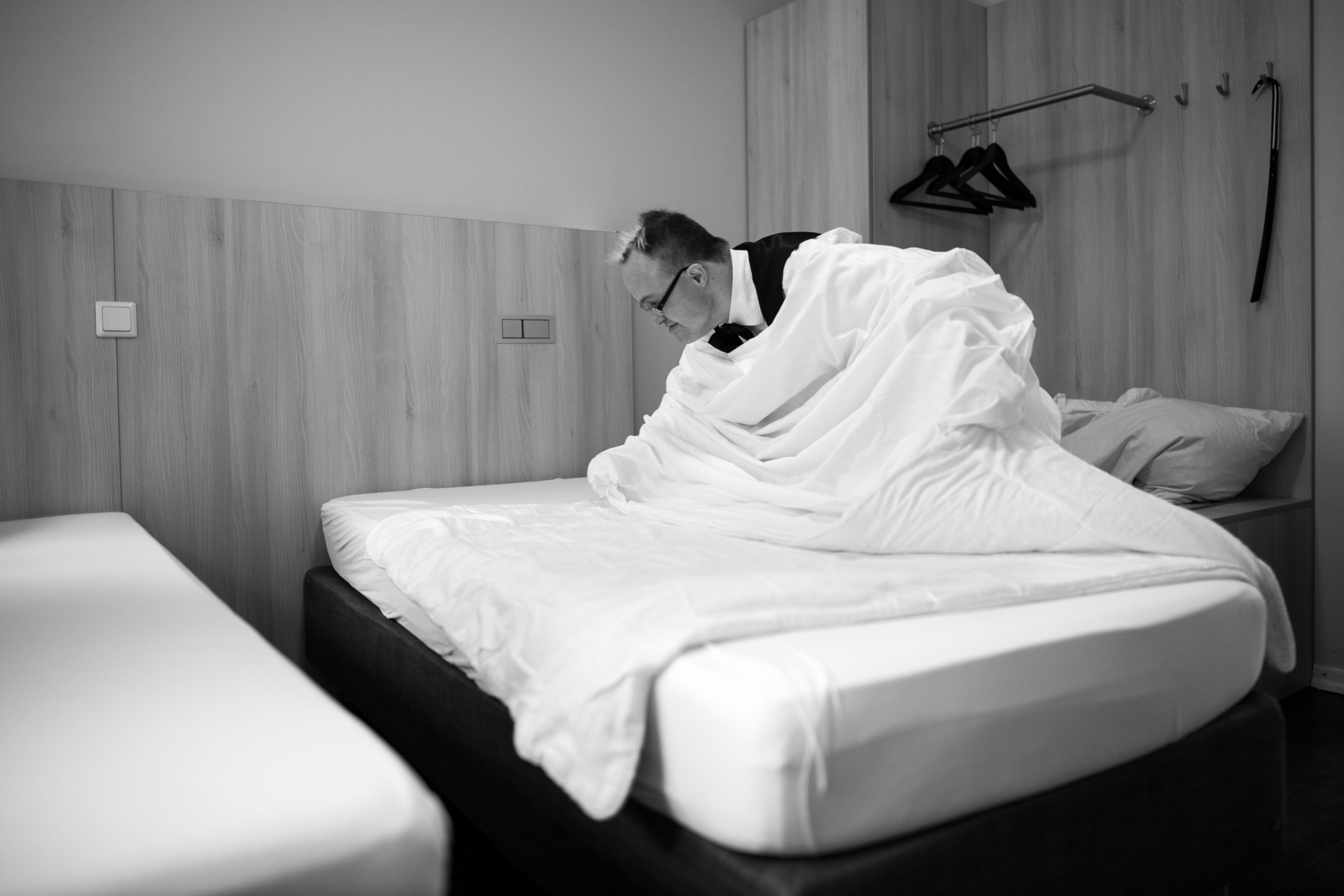 Ein Mann mit Trisomie 21 in einem Hotelzimmer beim Beziehen eines Bettes.