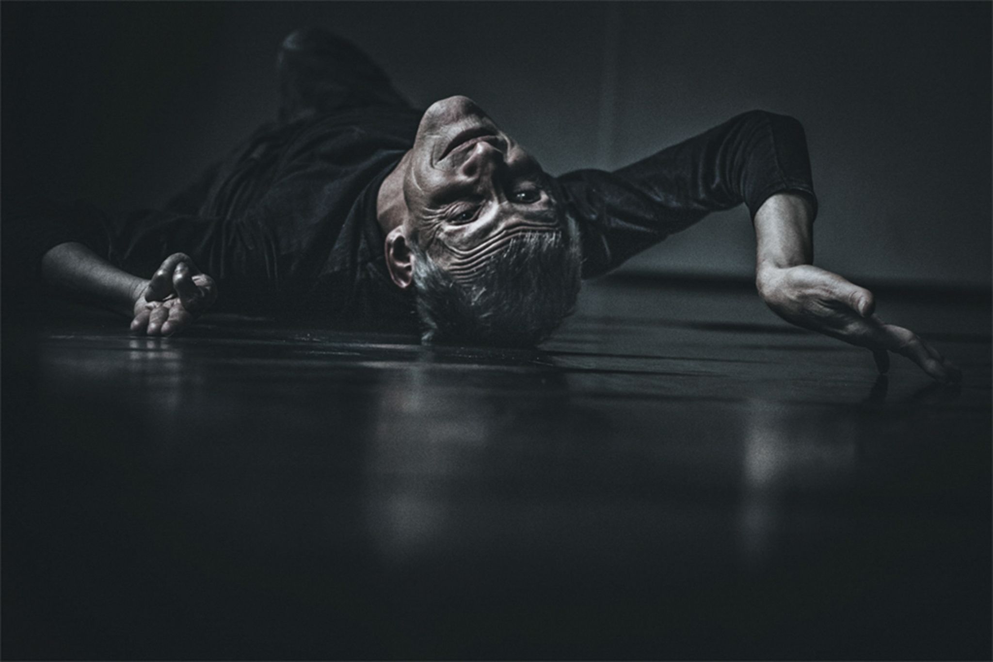 Ein spastisch gelähmter Mann liegt auf dem Rücken auf dem Boden eines dunklen Zimmers.