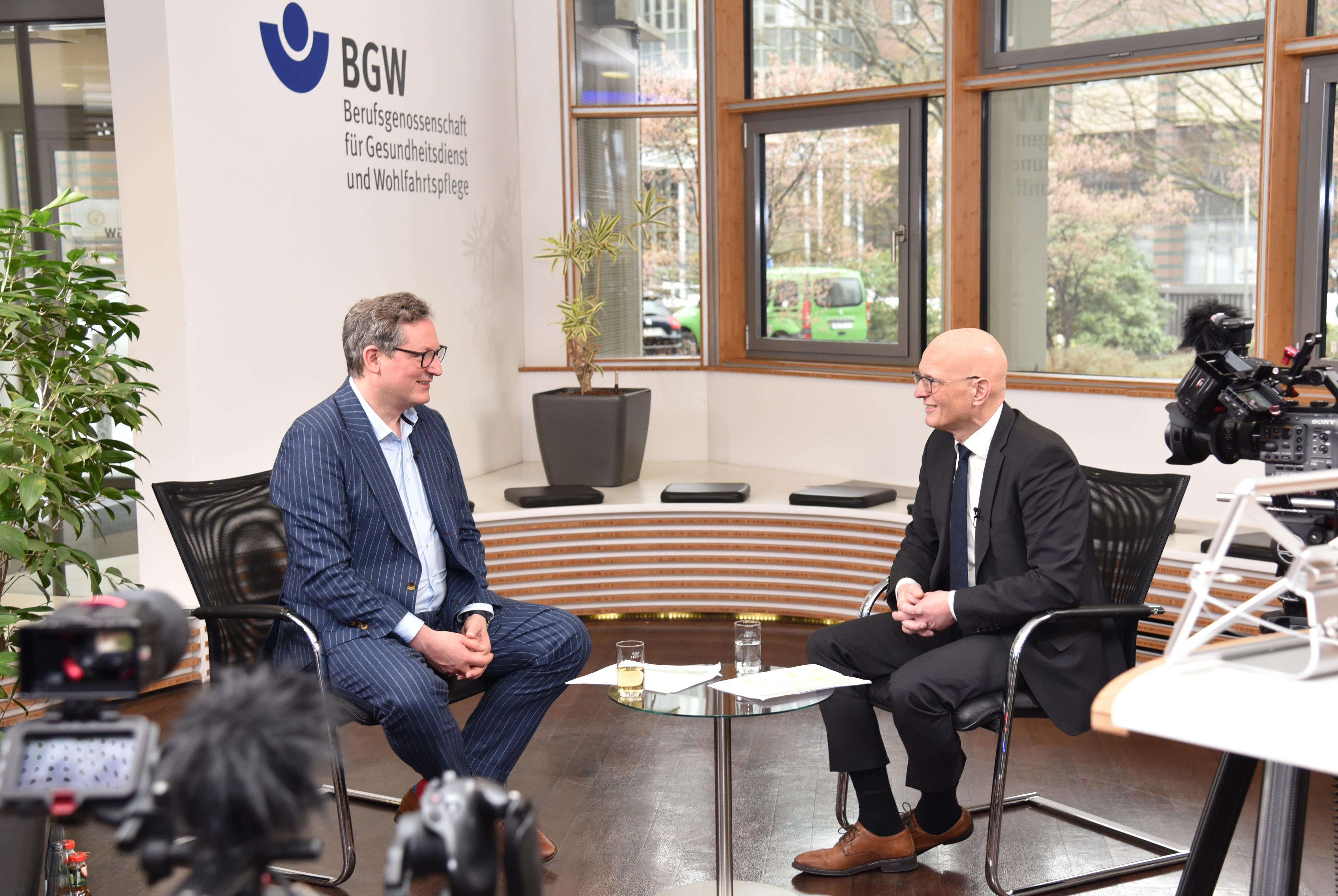  Dr. Eckart von Hirschhausen und BGW-Hauptgeschäftsführer Jörg Schudmann sitzen im Foyer der BGW-Hauptverwaltung und sprechen miteinander