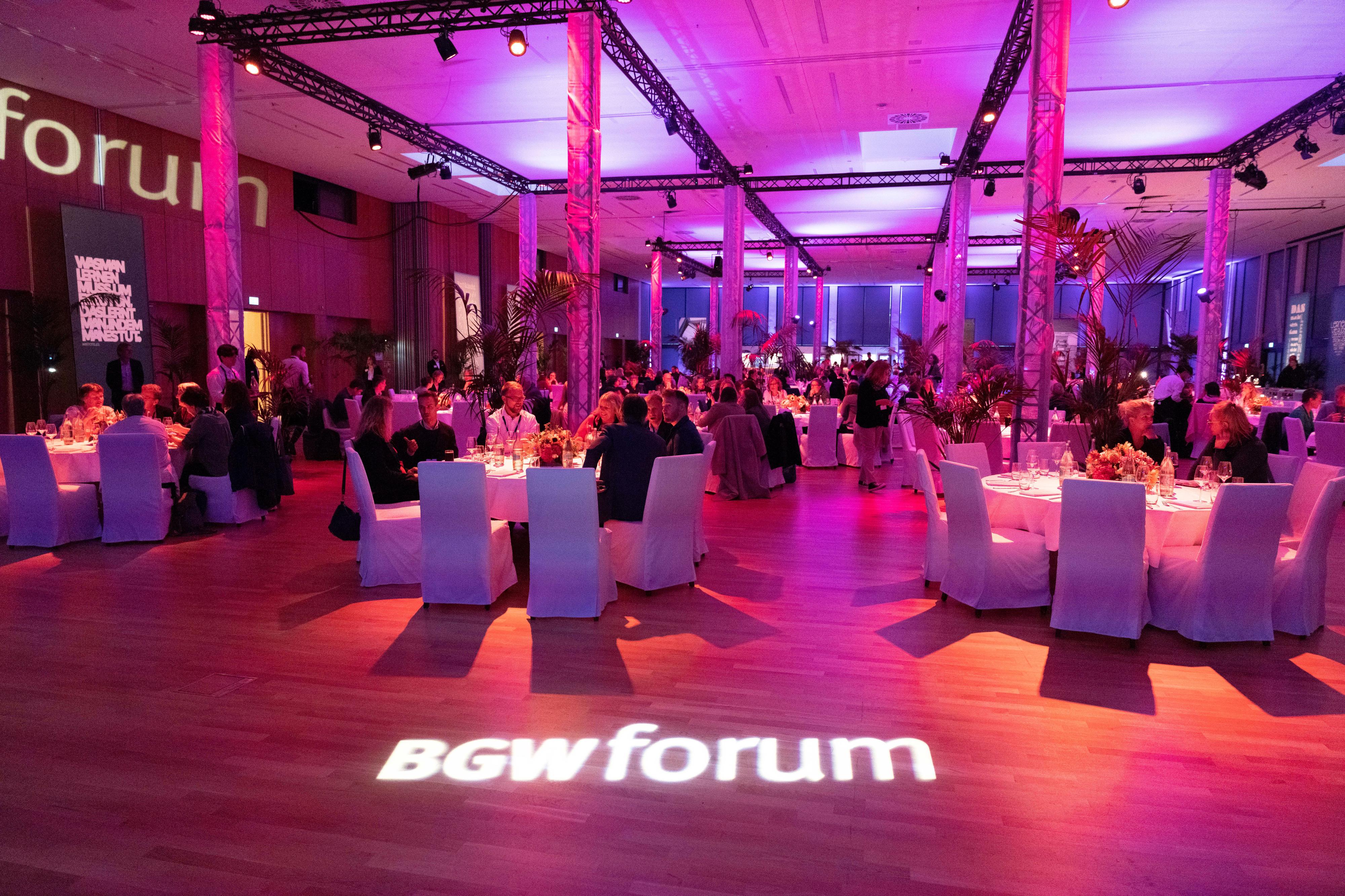 Netzwerkabend auf dem BGW forum: Menschen sitzen an gedeckten Tischen. Der Raum ist violett beleuchtet.