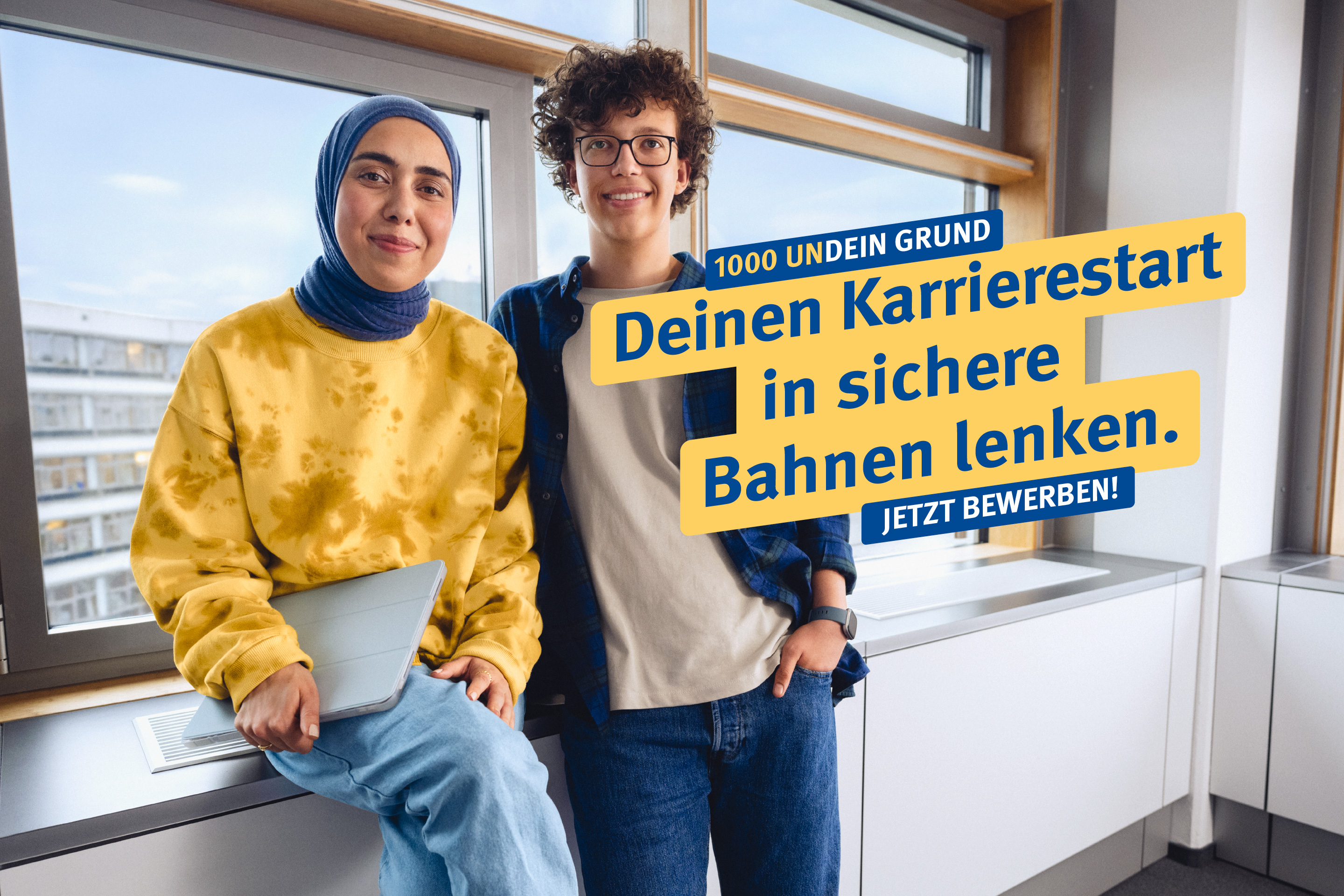 1000 UNDEIN GRUND – Deinen Karrierestart in sichere Bahnen lenken. Eine junge Frau und ein junger Mann stehen lächelnd vor einem Fenster im Büro, dazu der Text: "1000 undein Grund – Deinen Karrierestart in sichere Bahnen lenken. Jetzt bewerben!"