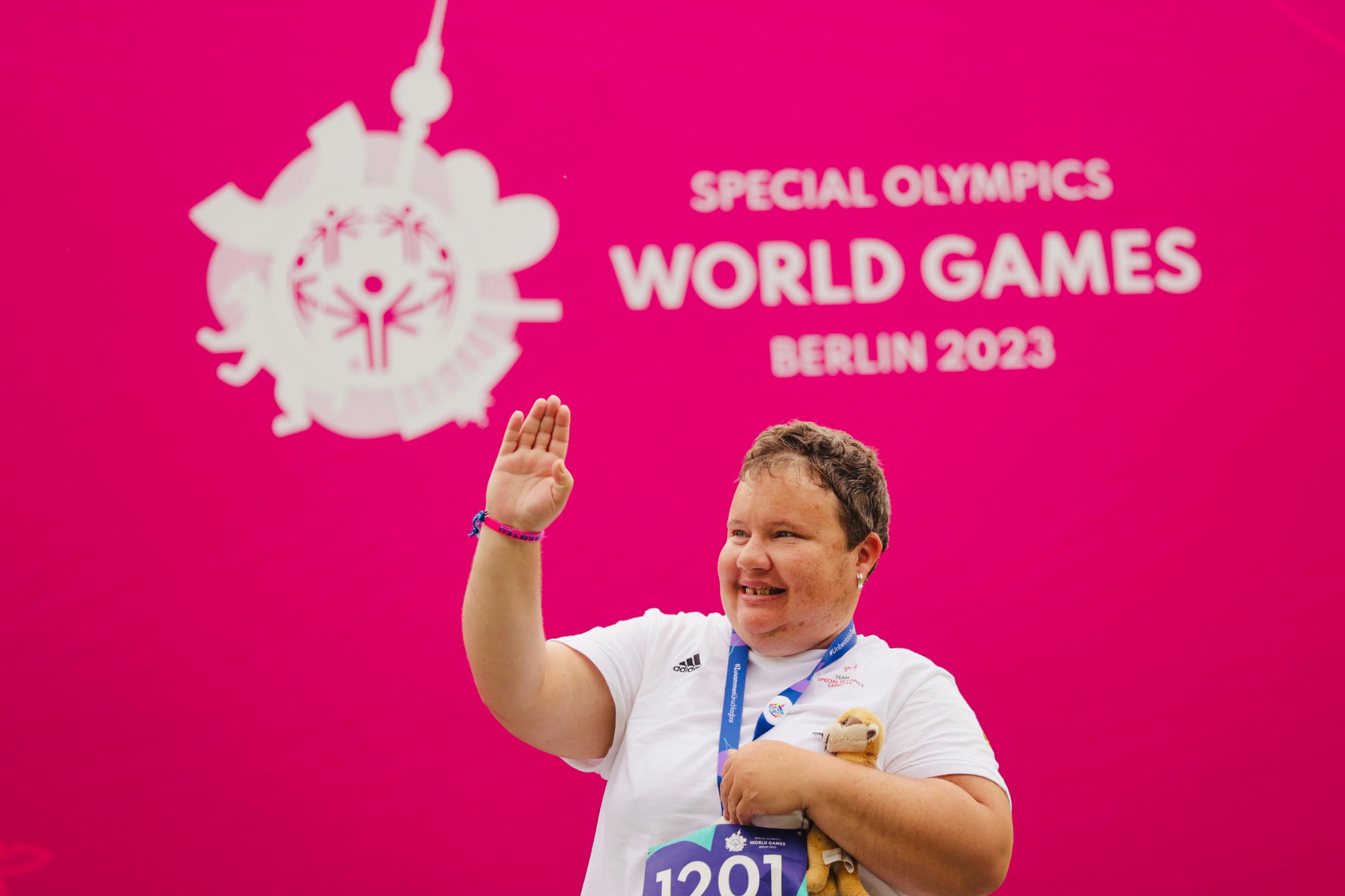 Miriam Klimetzek hat die Medaille um den Hals und hält sie mit einer Hand fest. Unterm Arm ein Kuscheltier, mit der anderen Hand grüßt sie.