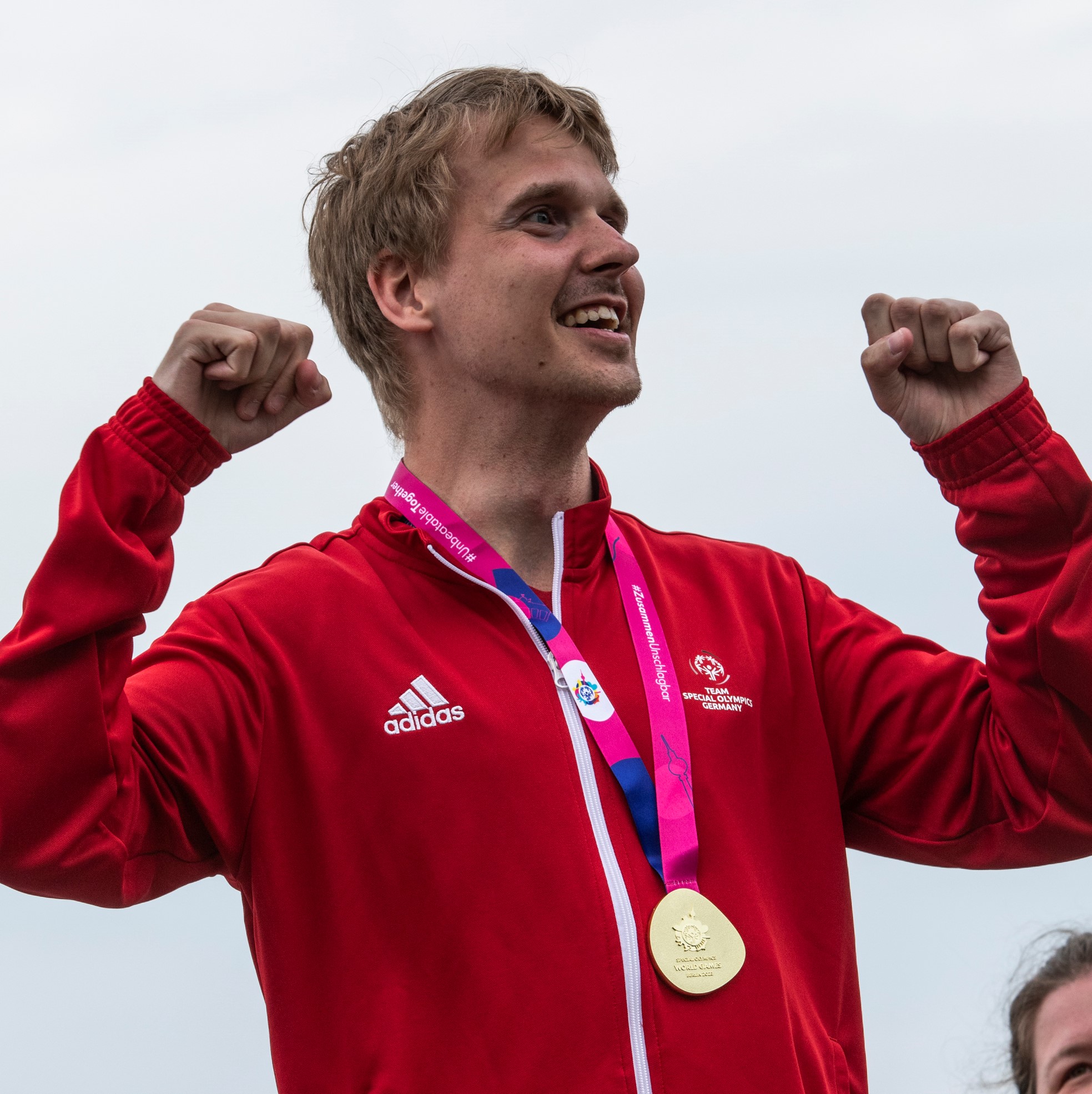 Kai-Jürgen Pönisch mit Goldmedaille in roter Trainingsjacke hebt in Siegerpose die Arme.