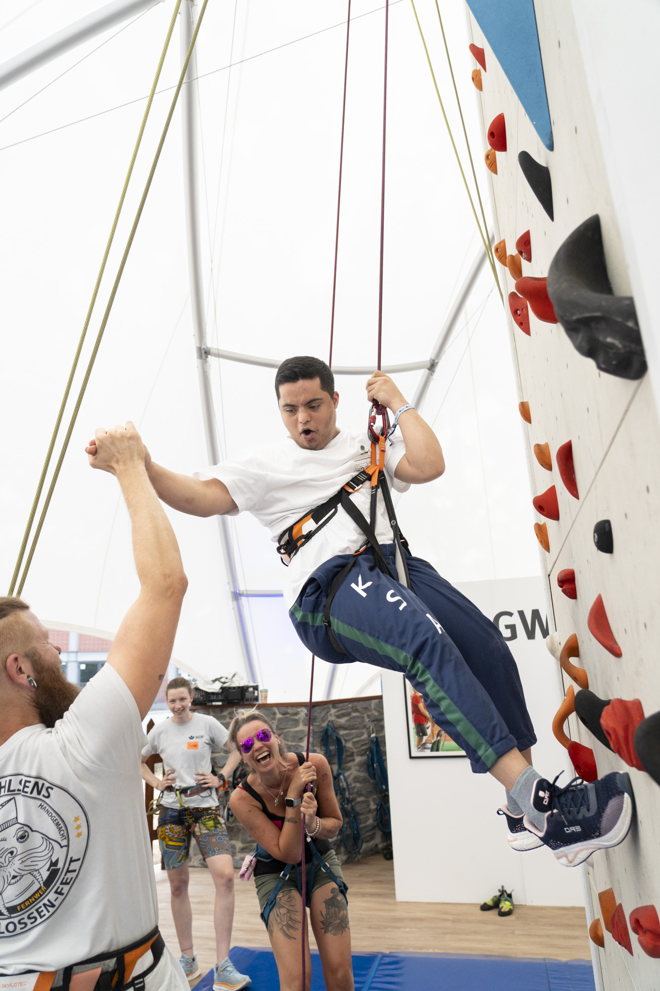 Ein junger Mann wird am Kletterturm abgeseilt. Eine Frau sichert ihn, ein Mann klatscht mit ihm ab.