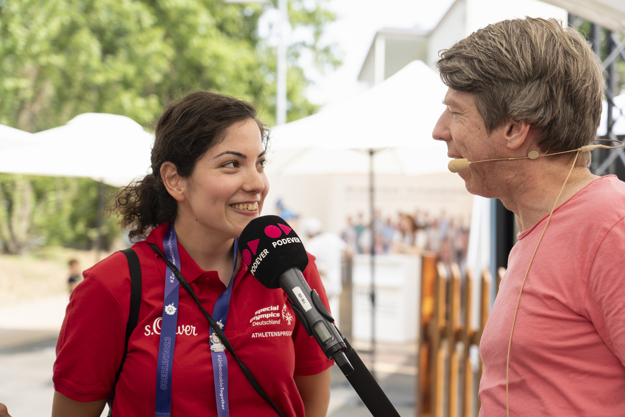 Mehtap Özgül steht neben Ralf Podszus, der ihr ein Mikrophon an den Mund hält. Im Hintergrund der BGW-Stand.