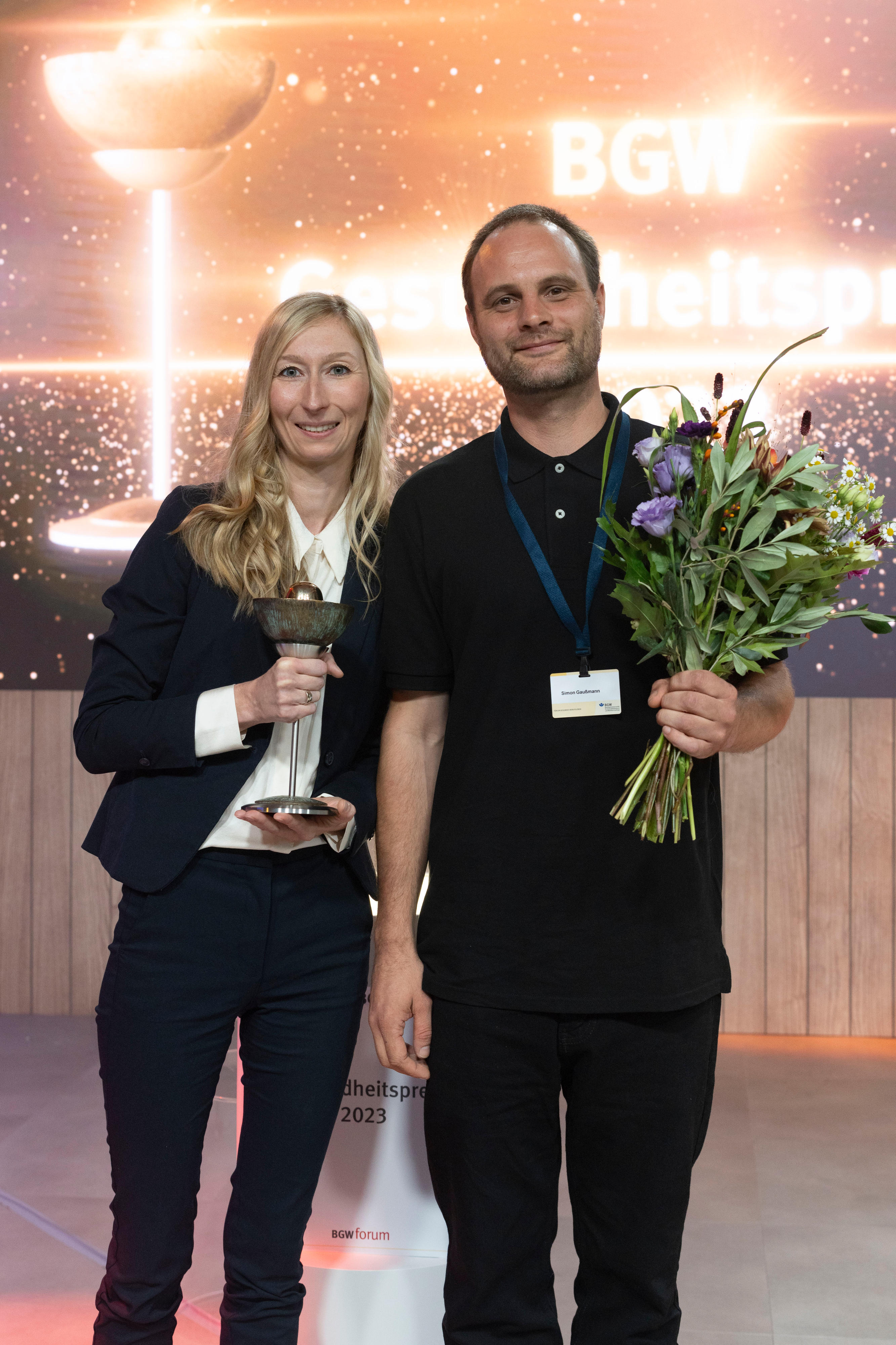 Nicole Schröder und Simon Gaußmann halten den Siegerpokal und Blumen in den Händen.