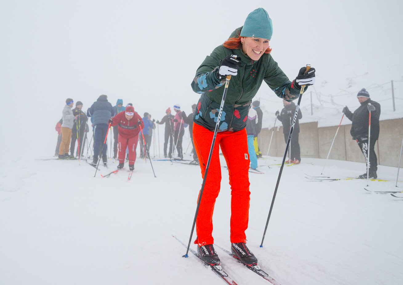 Eine Skilangläuferin auf Skiern im Schnee auf einer Skipiste. Im Hintergrund weitere Skifahrer.