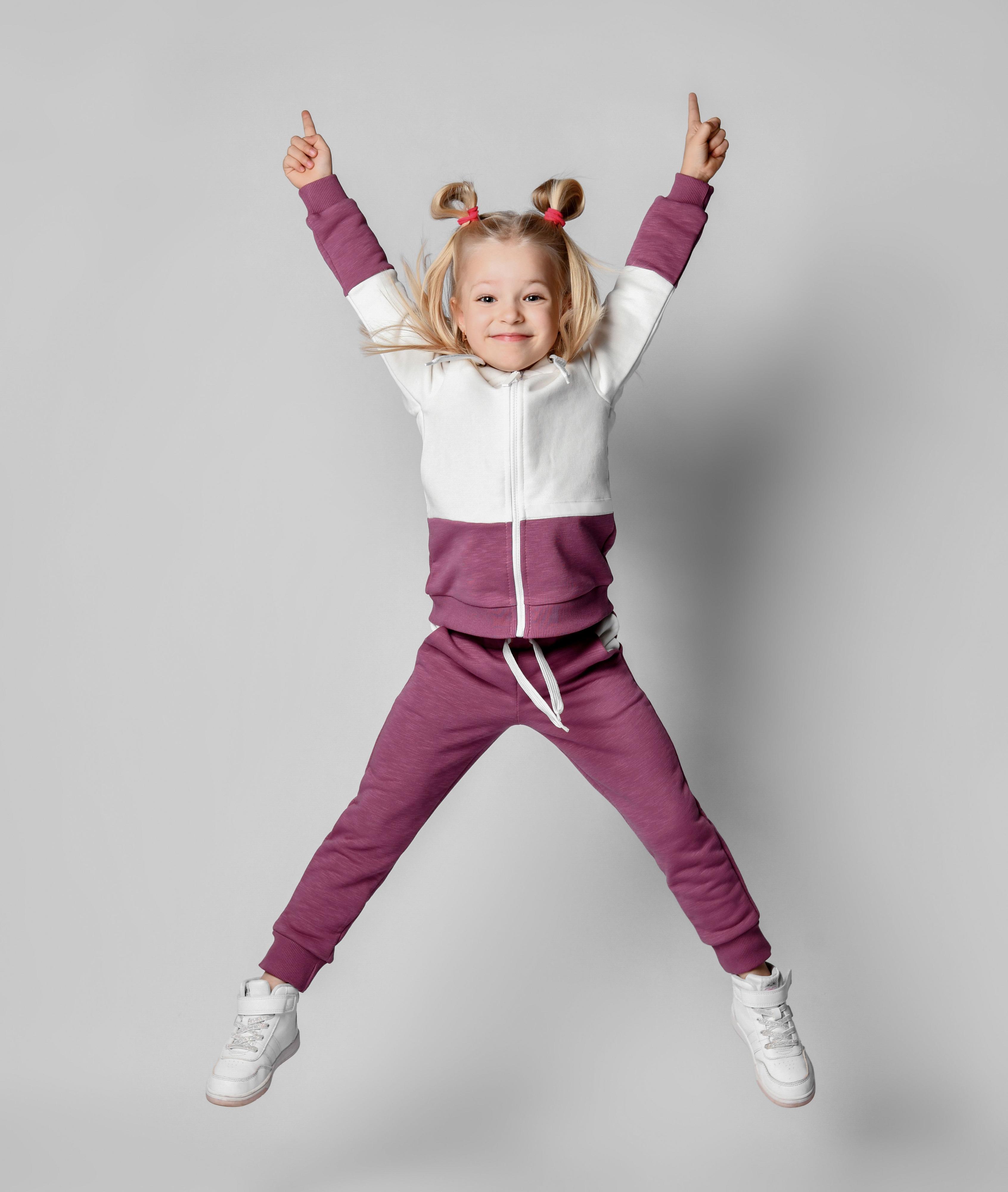 Kleines Mädchen im Jogging-Anzug mit Turnschuhen springt in die Luft
