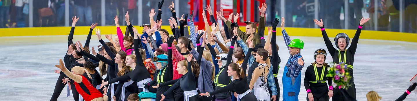 Special Olympics Nationale Spiele Thüringen 2024: Eisgala Eine Menschenmenge auf Schlittschuhen, die eng zusammen auf einer Eisfläche steht. Einige strecken die Arme hoch. Im Hintergrund Zuschauende hinter einer Abgrenzung.