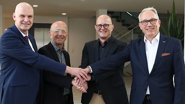 Die Verantwortlichen der vier Berufsgenossenschaften stehen nebeneinander und legen die Hände aufeinander