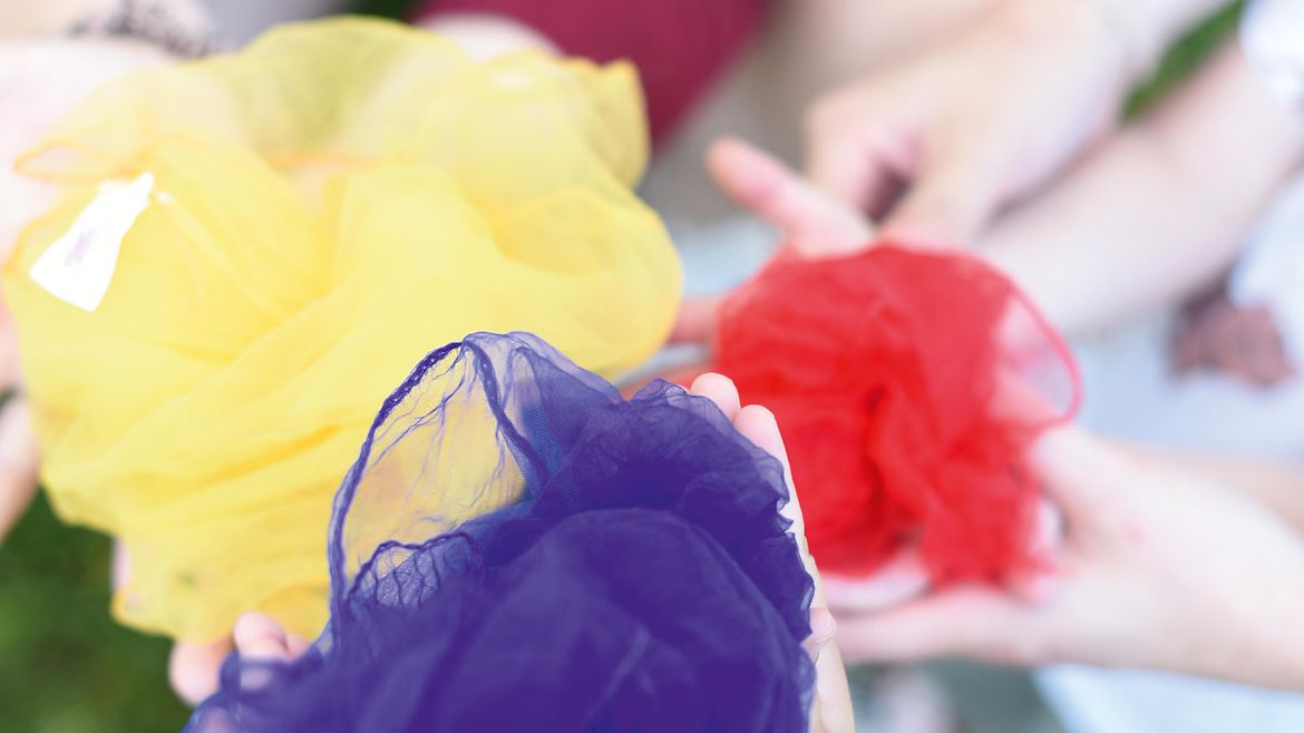Mehrere Kinder- und Erwachsenenhände halten bunte Tücher in die Kamera
