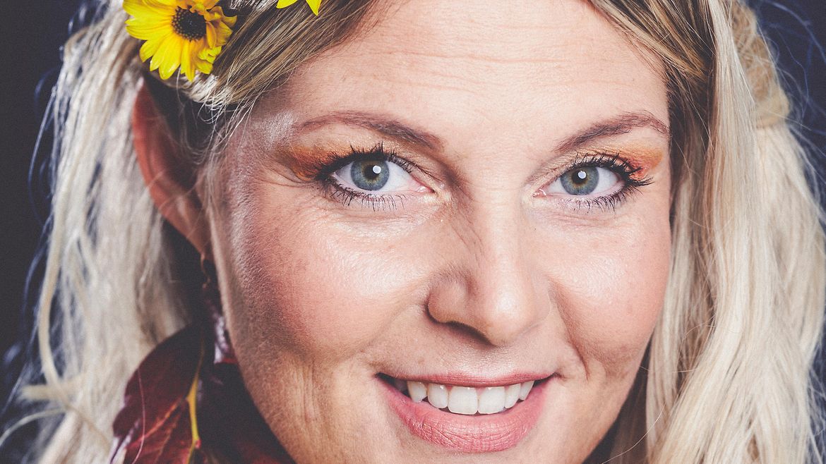 Porträt einer blonden, lächelnden Frau mit gelben und roten Blumen im Haar