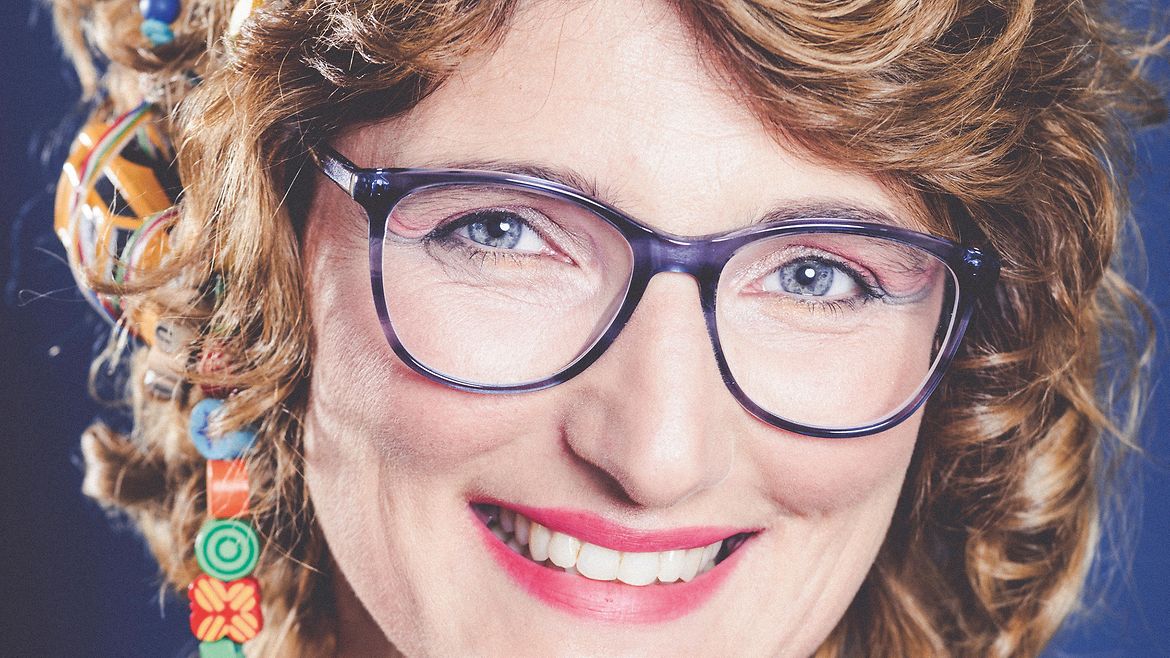 Porträt einer brünetten, lächelnden Frau mit einem Spielzeugauto und bunten Perlenketten im Haar