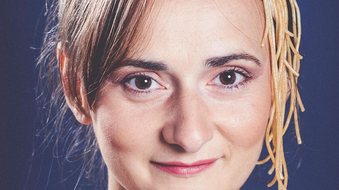 Porträt einer brünetten, lächelnden Frau mit Spaghetti und Tomaten im Haar