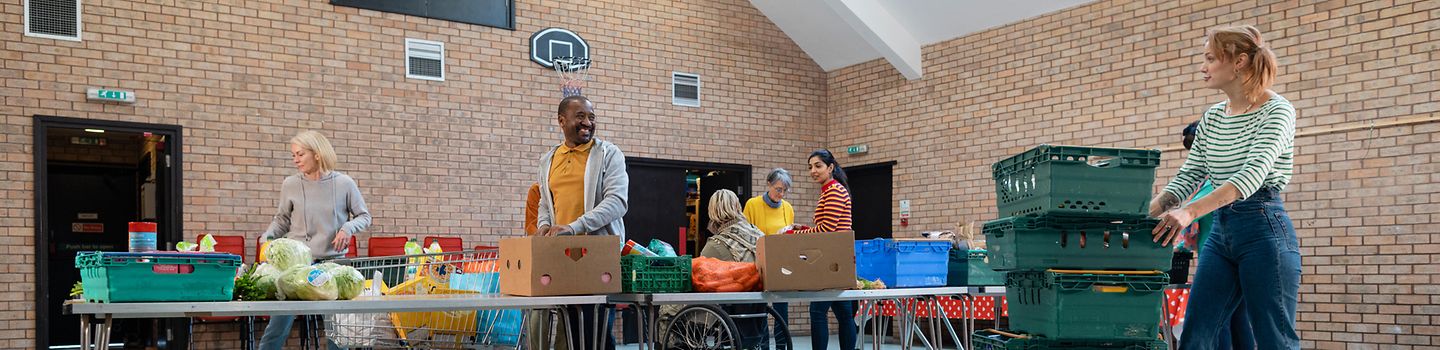 Lebensmittelausgabe In einer Turnhalle werden von Helfenden gespendete Lebensmittel zur Ausgabe aufgebaut.