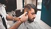 Ein Friseur rasiert am Kopf eines Kunden eine Linie.