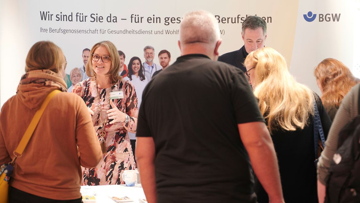 Mehrere Menschen stehen vor einem Messestand der BGW und schauen auf die ausgelegten Flyer und Broschüren.