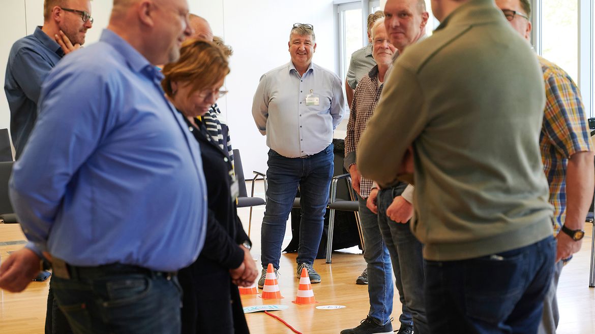 Eine Gruppe von menschen steht um einen roten Faden auf dem Fußboden herum. Daneben liegen Textschilder und kleine Pylonen.