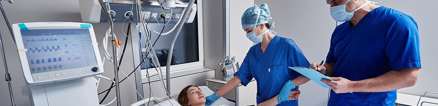 Pflegerin und Pfleger auf der Intensivstation mit Patientin. Intensivstaion mit Pflegerin und Pfleger neben einer Patientin im Bett.