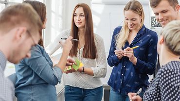 Vier Frauen und zwei Männer diskutieren miteinander und schreiben Ergebnisse auf Post-its.