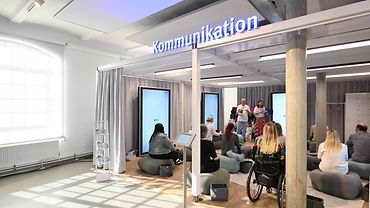 Menschen im Ausstellungsraum, über dem in großer Leuchtschrift "Kommunikation" steht
