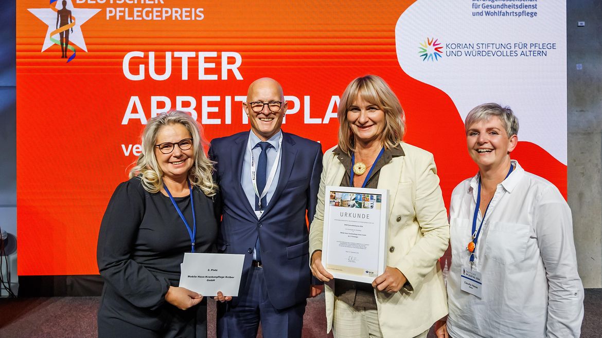 Jörg Schudmann, Hauptgeschäftsführer der BGW, zusammen mit Annett Dunger, Birgit Kröber, die die Urkunde hält, und Claudia Hesse vom der Mobilen Haus-Krankenpflege Kröber aus Zittau auf der Bühne. .