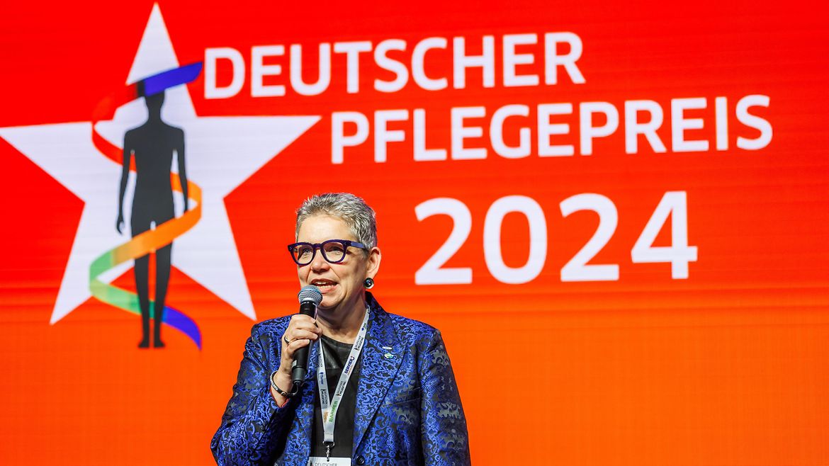 Eine lächelnde Frau mit Brille und Mikrofon und Namensschild um den Hals, auf dem Christine Vogler, Berlin steht.