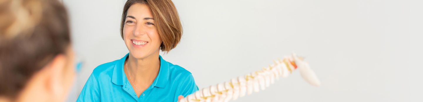Eine Ergotherapeutin zeigt einer Patientin ein Modell einer Wirbelsäule