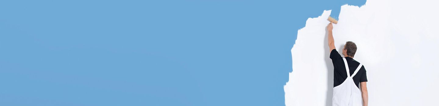 Maler steht auf Leiter und bemalt eine weiße Wand mit blauer Farbe, Ansicht von hinten