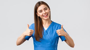 Krankenpflegerin Eine Krankenpflegerin in blauem Outfit lächelt und zeigt mit beiden Daumen nach oben.