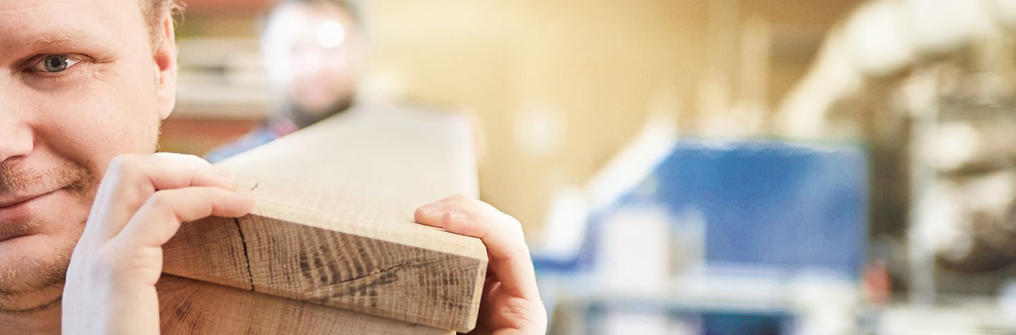 Werkstatt Zwei Männer in einer Holzwerkstatt tragen zwei lange, dicke und schwere Bretter auf ihren Schultern