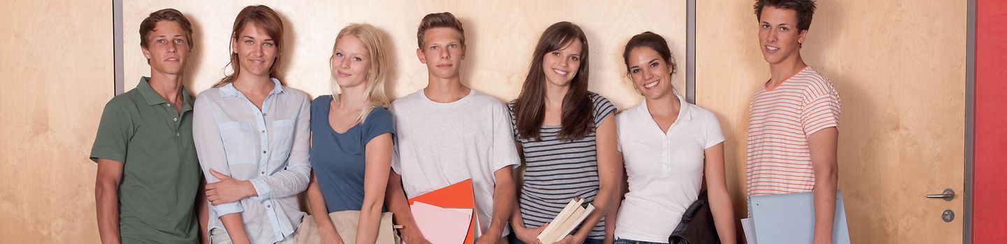 Sieben Schueler stehen an Wand gelehnt