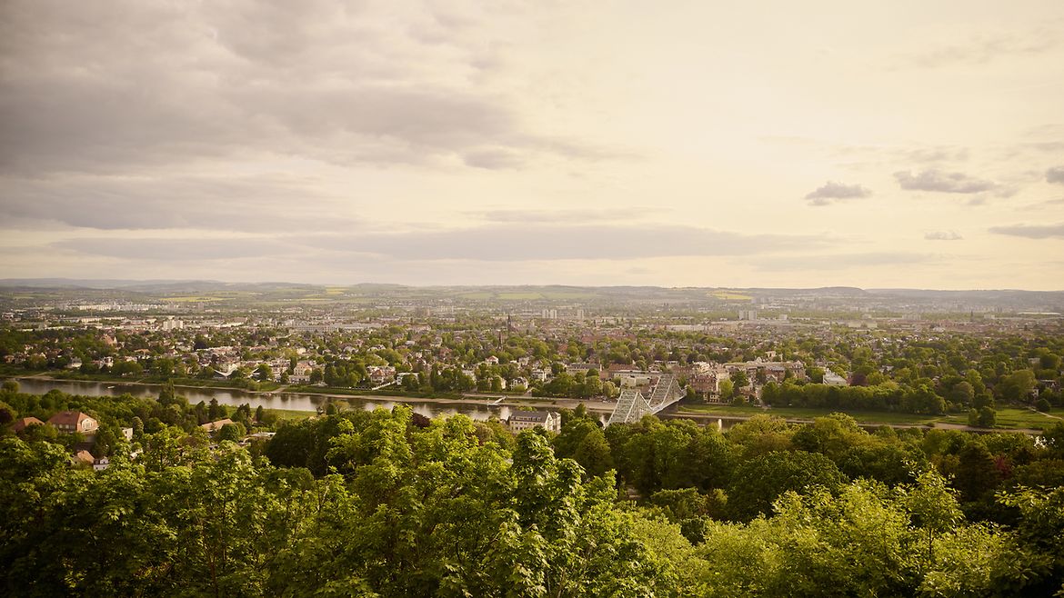 Blick auf einen Fluß mit einer Brücke und Stadt und grüne Landschaft dahinter.