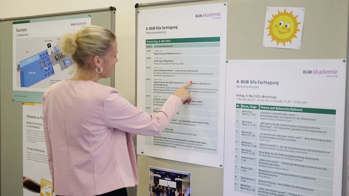 Eine Frau steht vor einer Stellwand mit einem Zeitplan der Sifa-Fachtagung.