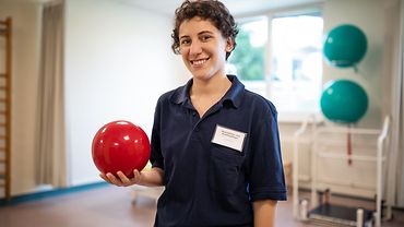 Physiotherapeutin mit Ball in Reha-Zentrum Eine Physiotherapeutin steht in einem Reha-Raum und hält einen kleinen Medizinball in der Hand