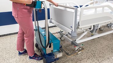 Eine Pflegekraft schiebt einen Bed Mover mit der Aufnahme unter ein Bett, um es anzudocken.