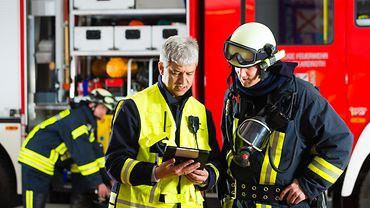 Zwei Feuerwehrmänner bei der Einsatzplanung Zwei Personen in Rettungswesten. Eine Person trägt einen Helm und Schutzbrille auf dem Kopf, um den Häls hängt ein Atemschutzgerät