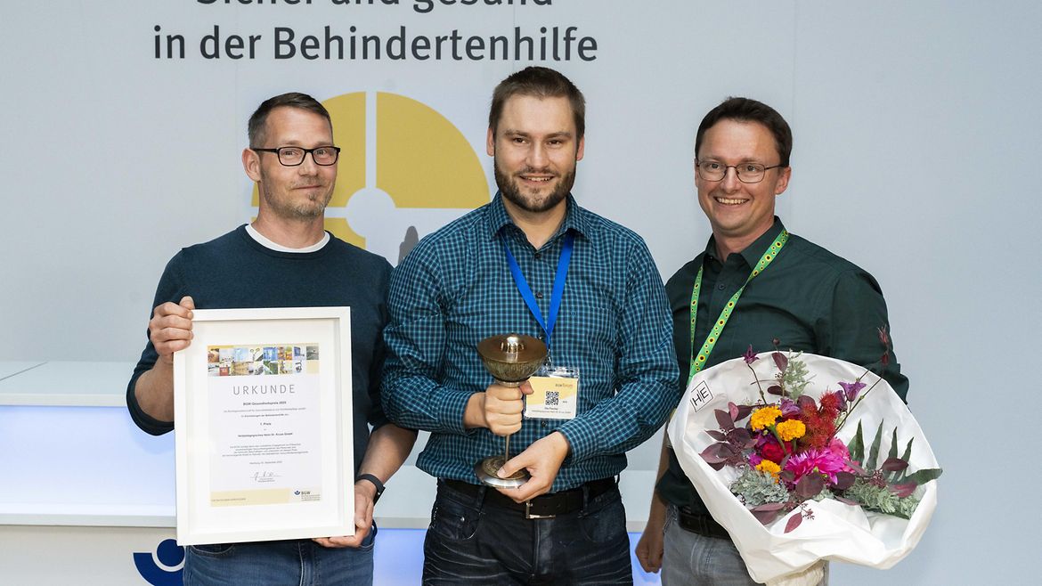 Moritz Kruse mit Urkunde, Bastian Kahn mit Pokal und Ole Fischer mit Blumenstrauß in den Händen, haben mit der Heilpädagogisches Heim Dr. Kruse GmbH aus Walsrode den 1. Preis gewonnen.