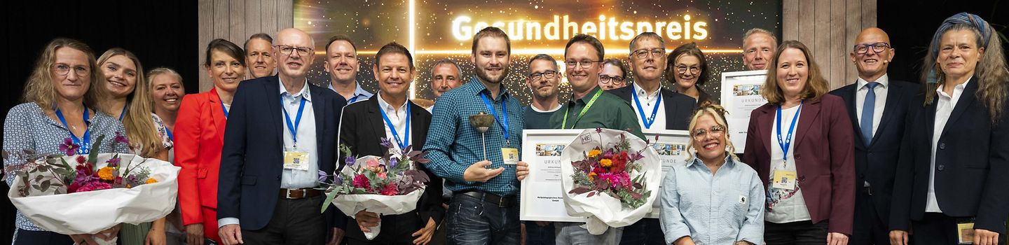 BGW forum 2025 "Sicher und gesund in der Behindertenhilfe" - Gesundheitspreis 2025 Gruppenbild der Finalteilnehmenden mit Jury-Mitgliedern und dem Hauptgeschäftsführer der BGW bei der Verleihung des BGW-Gesundheitspreises auf der Bühne.