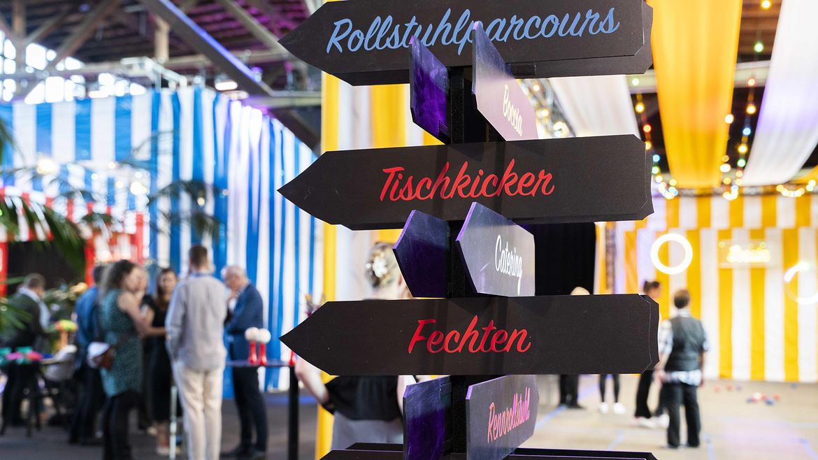 Hinweisschilder mit den Aufschriften "Rollstuhlparcours", "Tischkicker", "Fechten" , "Basketball"
