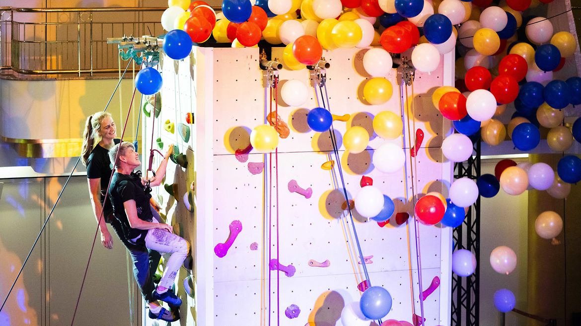 Zwei Personen am BGW-Kletterturm, an dem bunte Luftballons befestigt sind