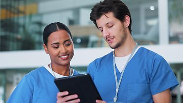 Eine Pflegerin und ein Pfleger in blauen Hemden schauen gemeinsam auf ein Tablet.