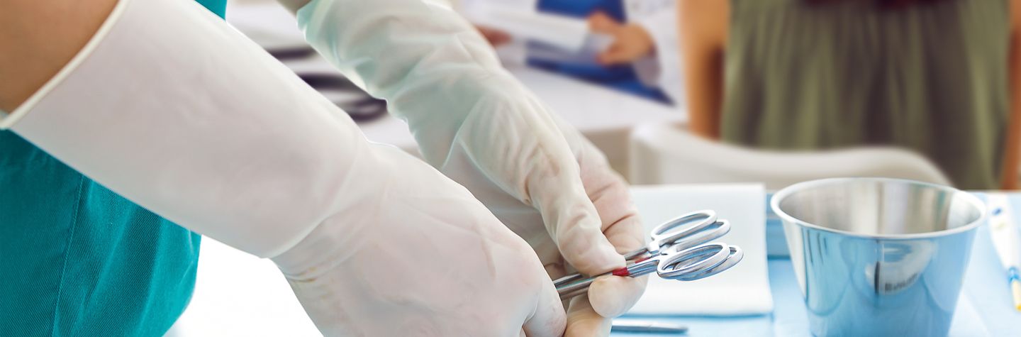 Arztpraxis Im Hintergrund eine Ärztin im Gespräch mit Patientin. Im Vordergrund legt eine Person medizinische Instrumente für einen kleinen operativen Eingriff bereit.