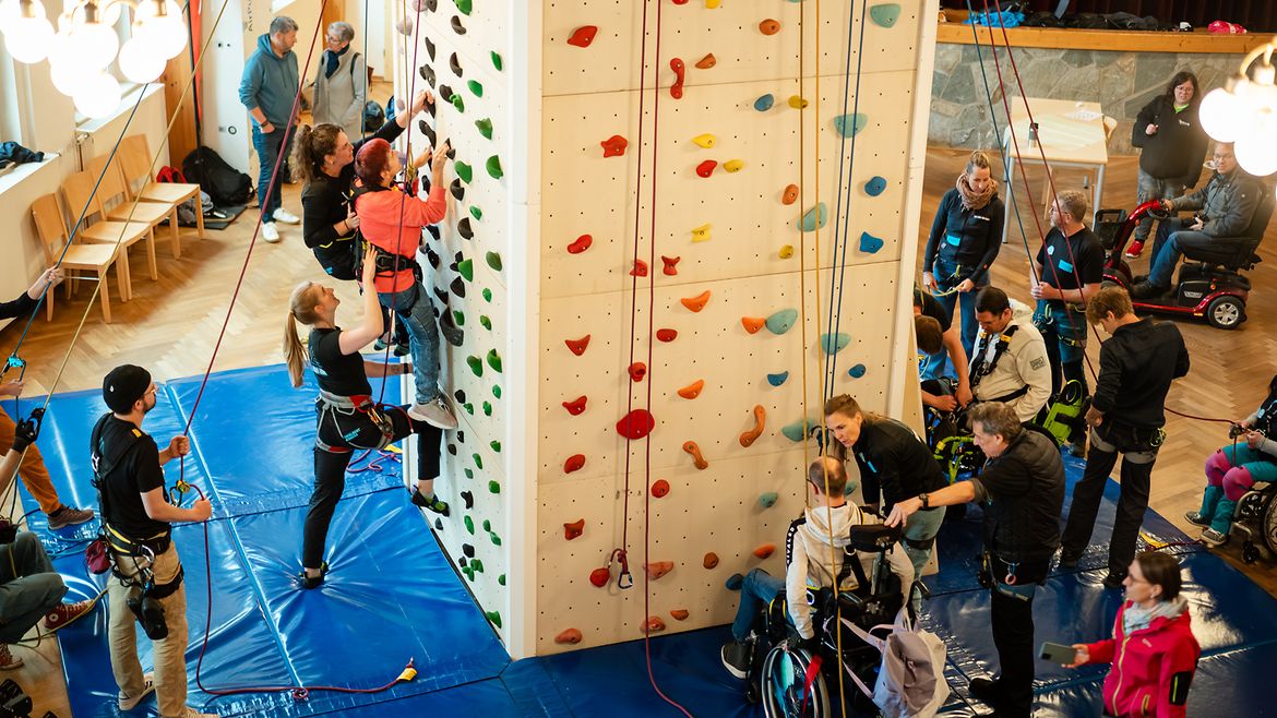 Fachkräfte begleiten Beschäftigte mit unterschiedlichen Beeinträchtigungen an der Kletterwand.
