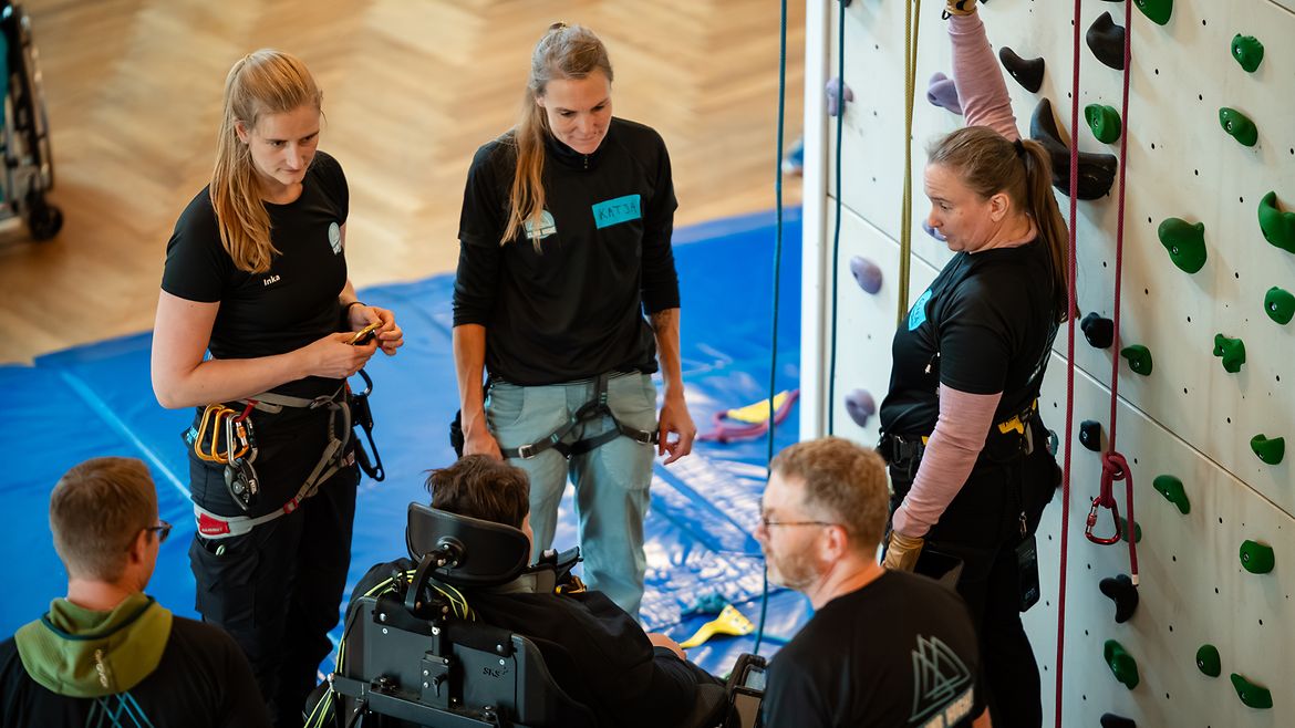 Fachkräfte erklären Beschäftigten mit Beeinträchtigungen den Einstieg in die Kletterwand.
