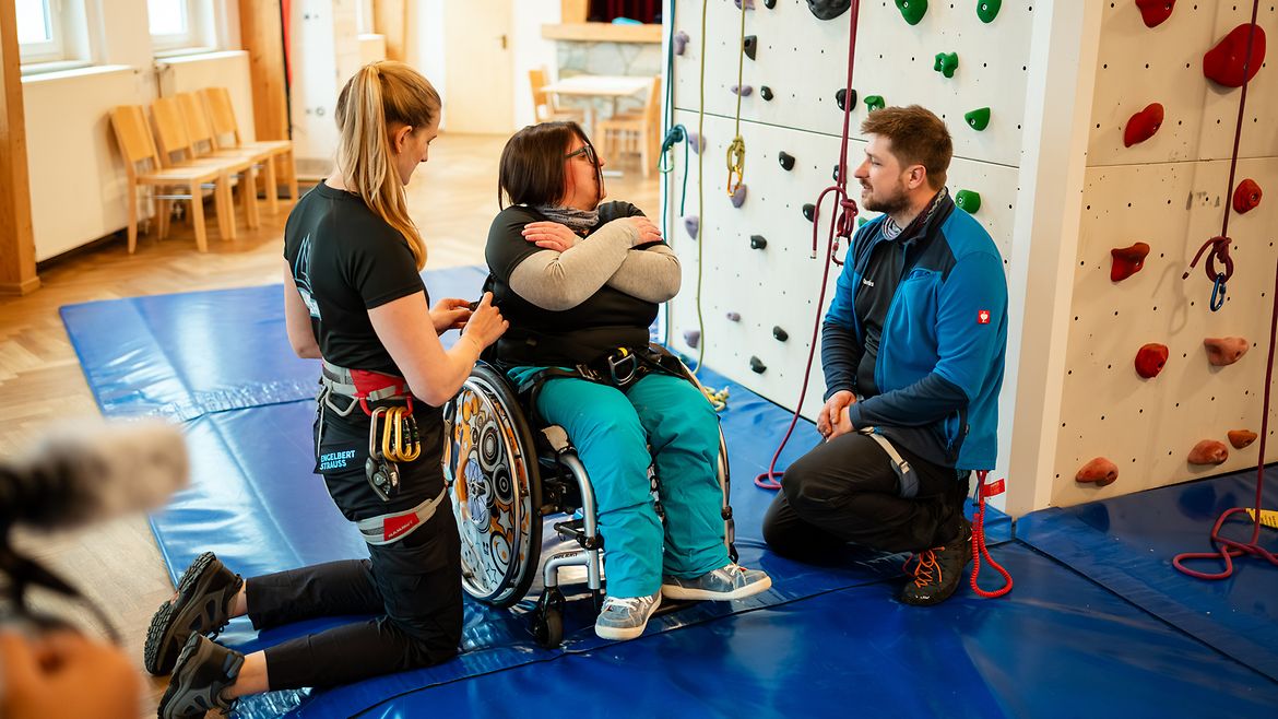 Zwie Fachkräfte erklären einer Beschäftigten mit Beeinträchtigung den Einstieg in den Kletterturm.
