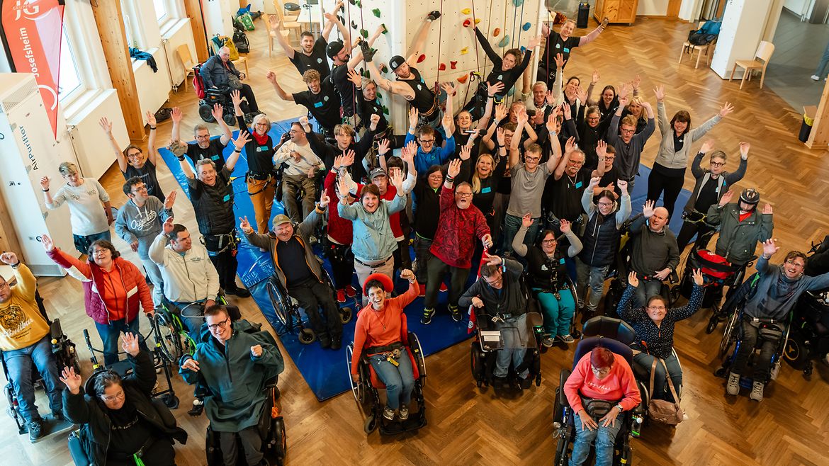 Teilnehmer winken vor dem Kletterturm in die Kamera.