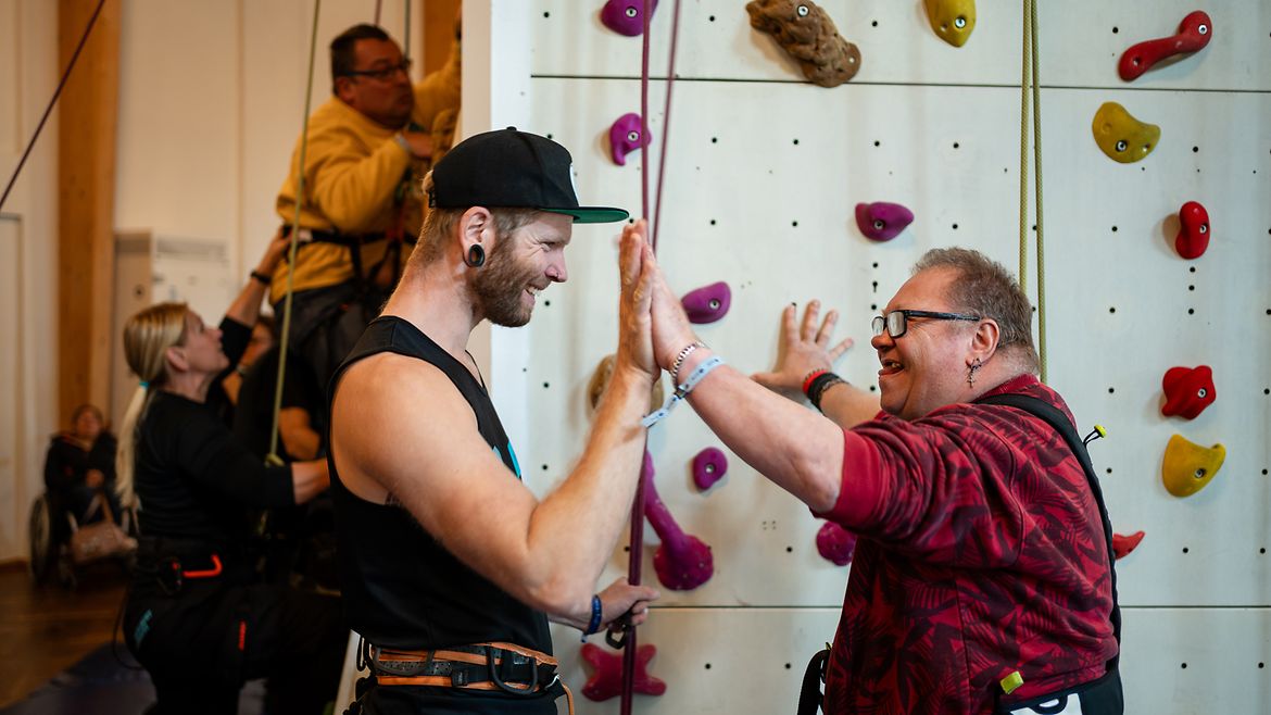 Zwei "Buddys" stehen vor der Kletterwand und halten die Hände aneinander.