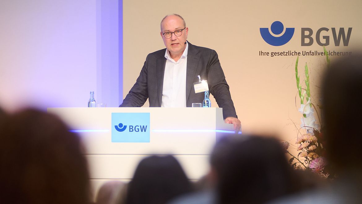 Blick aus dem Publikum zu einem Podium, an dem Rüdiger Schuch, Präsident der Diakonie Deutschland, steht und spricht.
