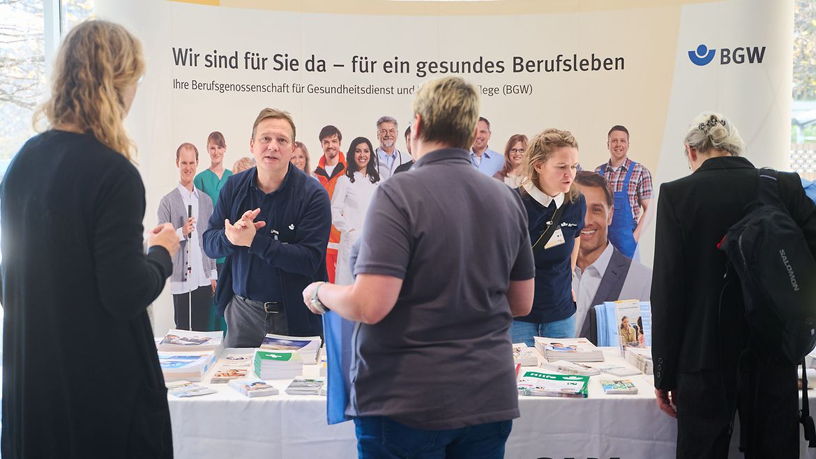 Menschen informieren sich an einem Messestand der BGW, es liegen Broschüren aus.